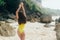 Backside view tanned girl resting at sandy beach with rocks on background