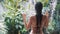 Backside view of woman in swimsuit takes shower, tropical greenery on background