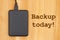 Backup today message with black portable hard drive with a cable