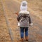 Backview of little girl in lightbrown short sheepskin coat, holding doll in park on cold day