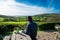 Backview young man in warm clothes sitting in farmer wooden cafe and enjoying local nature view with tea thermos on