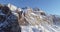 Backward aerial along snowy alpine steep rocky cliff valley.Sunny day,clear sky.Winter Dolomites Italian Alps mountains