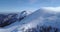 Backward aerial over winter snowy mountain top ski tracks resort with skier people skiing.Sunny day,foggy clouds.Fog