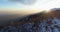 Backward aerial top view over winter snowy mountain and woods forest at sunset or sunrise.Dusk or dawn twilight sunshine