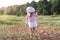 Backwards view of little girl in dress and white straw hat walking barefoot on sand at the sunset