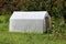 Backyard plastic greenhouse with metal doors covered with white nylon and surrounded with high uncut green grass and tall trees
