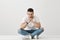 Bad days come and go. Indoor shot of gloomy thoughtful young man in glasses sitting on floor with crossed legs, leaning