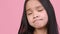 Bad idea. Close up portrait of doubtful little asian girl pondering, feeling unsure, pink studio background