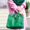 Bag close-up in female hands. Stylish modern and feminine image, style. Girl with a green bag in a pink coat