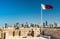 Bahrain Flag with skyline of Manama at Bahrain Fort. A UNESCO World Heritage Site