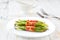 Baked bundles of green beans wrapped in bacon in a ceramic plate on a white wooden table, close up