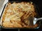 Baked cheesy penne pasta in glass container on stove with spatula