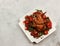 Baked chicken with lentils, Ñherry tomatoes, and scallions on a white rectangular plate on a light gray background.