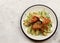 Baked chicken with potatoes and scallions on a white round plate on a light gray background.