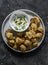 Baked crispy parmesan bread crumbs cauliflower bites with yogurt sauce on dark background, top view