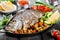 Baked dorado fish with vegetables and lemon on pan on wooden background close up