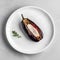 Baked eggplant on a white plate on a marble background.