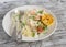 Baked fish with lemon and herbs and cous cous on a white plate, on bright wooden surface.