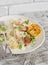 Baked fish with lemon and herbs and cous cous on a white plate, on bright wooden surface.