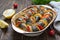 Baked fish with vegetables. Pieces of herring, onions, tomato, lemon, aromatic herbs in ceramic form on a rustic wooden table