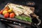 Baked Haddock fish fillet on wooden board with tomato and potato. Black background. Top view