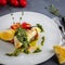 Baked Halibut fish steak with lemon, carrot and sauce salsa verde. White plate, thyme, spoon, fork on the grey background. Close-