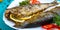 Baked herring with lemon and spices on a white plate on a wooden table. Tasty fish dish. Top view