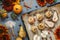 Baked pears and apples on baking pan with spices, little pumpkins and flowers around on grey table