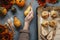 Baked pears and apples on baking pan with spices, little pumpkins and flowers around on grey table