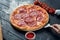 Baked pizza with salami chorizo with red sauce and melted cheese on a black wooden background in a composition with ingredients.