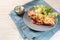 Baked pointed bell pepper stuffed with rice, tuna, tomatoes and cheese on a blue plate with lettuce salad, dip and parsley garnish