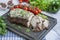 Baked pork chopped in a walnut and mint sauce on a cutting board with fresh herbs and vegetables. Light background