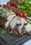 Baked pork chopped in a walnut and mint sauce on a cutting board with fresh herbs and vegetables. Light background