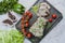 Baked pork chopped in a walnut and mint sauce on a cutting board with fresh herbs and vegetables. Light background