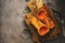 Baked pumpkin or butternut squash with herbs on a cutting board, dark rustic background, flat lay, top view