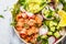 Baked red fish salad with avocado, cucumber, radish and arugula in white plate, top view