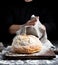 Baked round bread on a board behind the cook in black clothes