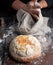 Baked round bread on a board, behind the cook in black clothes