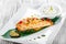 Baked salmon with cheese sauce, rosemary and lemon on wooden background. Hot fish dish.