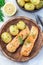 Baked salmon in creamy sauce with young boiled  potato topped with melted butter and chopped dill on wooden plate, vertical, top