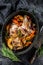 Baked whole lamb shoulder leg in a baking dish. Black background. Top view