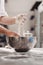 Baker adds flour to dough in an iron bowl on the table in the bakery