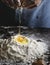 Baker breaking an egg into a flour mixture