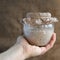 Baker hand holds glass jar with rye sourdough on brown sackcloth background, leaven starter for organic rustic bread