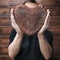 Baker hands gently holds rye whole grain sourdough bread in shape of heart in front of face, faceless, square frame