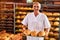 Baker holds a tray with fresh hot bread in his hands against background of shelves with pastries in bakery. Industrial production