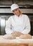 Baker kneading dough in bakery or bakehouse