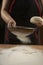 Baker pours flour for making pizza. Chef cooking dough to bake a cake on a wooden table.