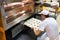 Baker puts tray of dough balls to bake buns into oven