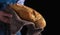 Baker`s hands hold fresh bread over dark background